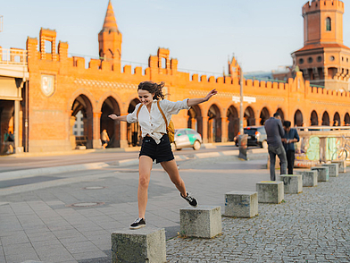 Schülerin springt über Steine an der Oberbaumbrücke – Deutsch Sprachreise Berlin für Jugendliche