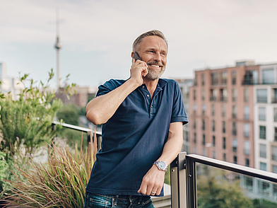 Geschäftsmann telefoniert auf Balkon mit Blick über Berlin – Business Deutsch Alltagssituation