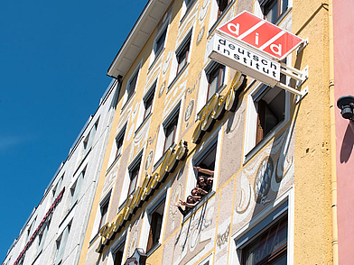 Facciata di una scuola di lingue a Monaco con studenti che salutano allegramente dalle finestre