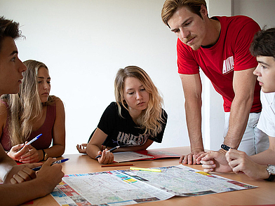 Lehrkraft unterstützt Lernende beim gemeinsamen Arbeiten mit Stadtplan im Unterricht