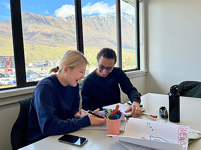 Zwei Schüler lernen lachend im Klassenzimmer mit Blick auf die Remarkables-Berge in Queenstown.