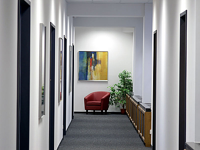 Moderner Flur mit weißen Wänden, Kunstwerken und einer roten Sitzgelegenheit am Ende des Gangs