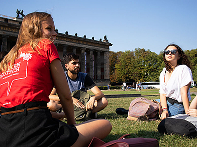 Lernende sitzen gemeinsam auf einer Wiese und üben Deutsch im Gespräch