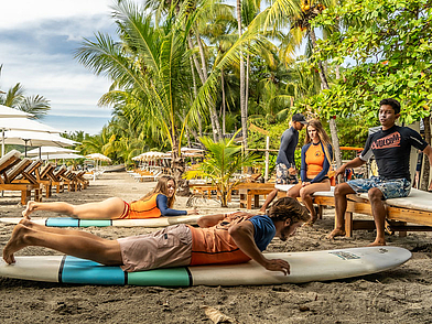 Surfanfänger üben Paddel- und Aufstehbewegungen auf Surfboards im Sand vor der Expanish Sprachschule Sámara.