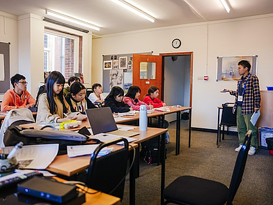 Lehrer erklärt während des Unterrichts an der Tafel, während Jugendliche aufmerksam zuhören und Notizen machen – Sprachschule St. Giles Canterbury.