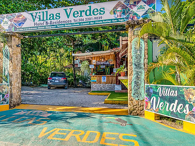 Eingang zu den Villas Verdes in Sámara mit Rezeption, tropischer Vegetation und Hotelbeschilderung.
