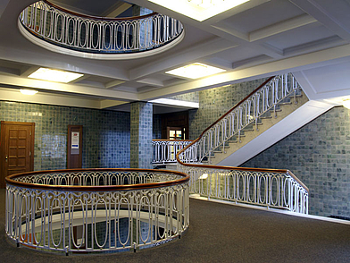 Helles Treppenhaus mit geschwungener Balustrade und mehreren Etagen in einem historischen Schulgebäude