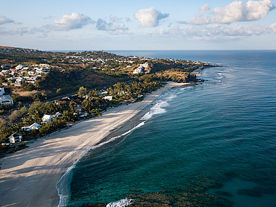 Weitläufiger Sandstrand mit Blick auf die Küste von Saint-Paul auf La Réunion, gesäumt von Häusern und tropischer Vegetation – eine traumhafte Kulisse für Französisch-Sprachreisen.