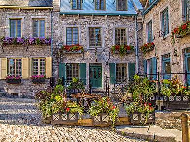 Historische Altstadtgasse in Québec mit Steinfassaden und Blumen, die Sprachreisende beim Erkunden der Stadt entdecken.