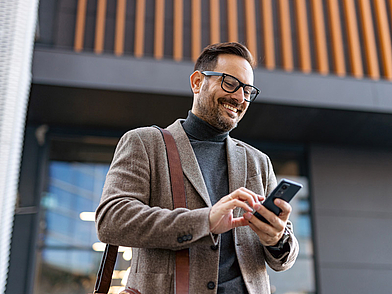 Geschäftsmann in Frankfurt, der unterwegs auf sein Smartphone schaut – symbolisiert modernes Arbeiten und berufliche Weiterbildung im Rahmen von Business-Deutsch-Sprachreisen
