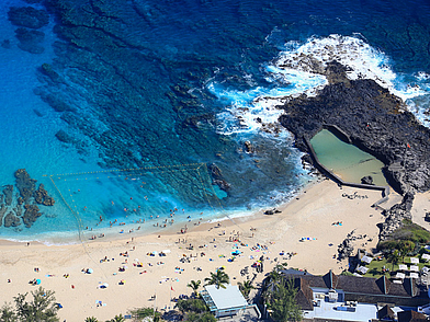 Luftaufnahme vom Strand in Saint-Paul auf La Réunion mit türkisblauem Wasser, natürlichen Felsformationen und einem kleinen Naturpool, ideal für Sprachreisen in exotischer Umgebung.