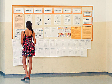 Teilnehmerin liest den Wochenplan am schwarzen Brett der Schüler Sprachschule Wien.