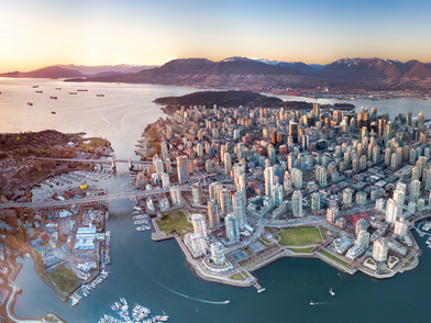 Vista aerea di Vancouver con lo skyline densamente edificato, il porto e le montagne circostanti al tramonto