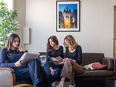 Sprachreisende entspannen in der Lounge und blättern durch Kursunterlagen – Begegnungsbereich in Bordeaux.