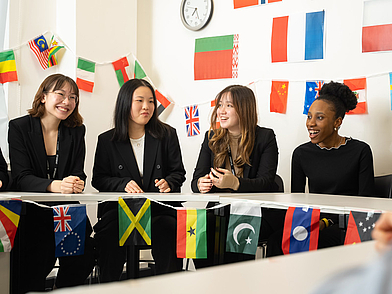 Internationale Schülergruppe der St. Giles Sprachschule Oxford lacht gemeinsam in einem mit Flaggen dekorierten Raum.