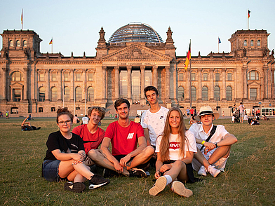 Gruppe Jugendlicher sitzt entspannt auf einer Wiese vor dem Reichstag bei Sonnenuntergang