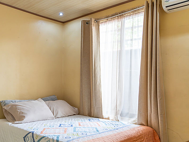 Ein Schlafzimmer in einer Gastfamilie in Sámara mit Doppelbett, heller Bettwäsche und Tageslicht durch das Fenster.