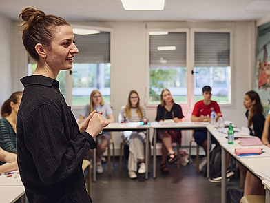 Lehrerin der Sprachschule Ifalpes Annecy leitet eine Französischstunde, während motivierte Sprachschüler aufmerksam zuhören und aktiv teilnehmen.