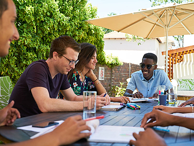 Internationale Sprachschüler lernen gemeinsam an einem Tisch im Außenbereich der Schule.
