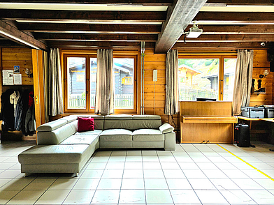 Aufenthaltsraum im Chalet der Sprachschule friLingue Liddes mit Sofa und Klavier – Treffpunkt für Schüler.