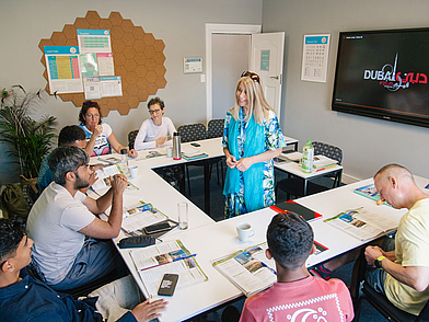 Lehrerin unterrichtet eine kleine internationale Gruppe von Sprachschülern in einem hellen Klassenraum während einer Englischstunde.
