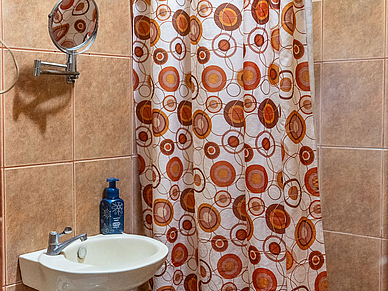 Kleines Badezimmer einer Gastfamilie in Sámara mit Waschbecken, Wandspiegel und Duschvorhang mit orangefarbenem Muster.