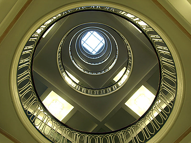 Blick nach oben durch ein rundes Treppenhaus mit mehreren Etagen und Glasdach