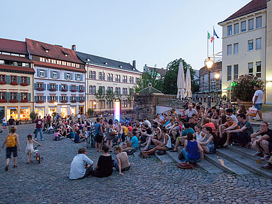 Junge Leute sitzen in den Abendstunden auf den Stufen eines Freiburger Platzes, lebendige Atmosphäre einer Sprachreise in Deutschland.
