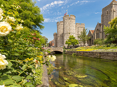 Blühende Uferpromenade und historische Westgate Towers in Canterbury – beliebt bei Sprachschülern für Spaziergänge.