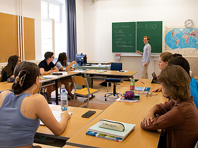 Deutschlehrerin erklärt Schülern Grammatik an der Tafel während des Unterrichts in Wien.